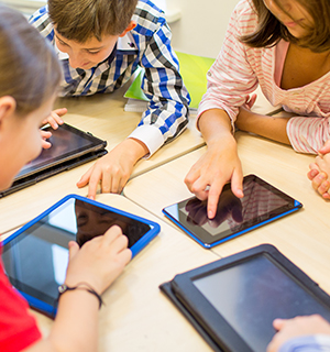 Happy elementary students working together with their tablet computers